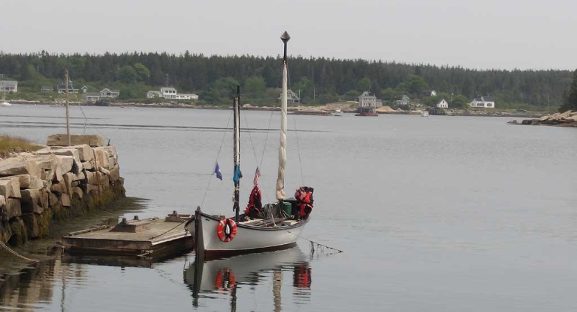 a sailboat tethered to a small dock float on calm water. 